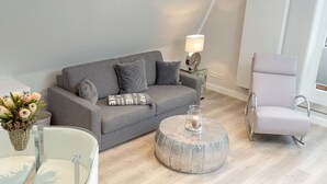 A modern living room with a grey sofa, a round coffee table, and a white armchair. - Penthouse maisonette Lagmöwe (Westerland)