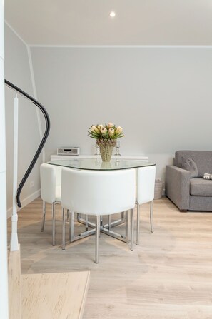A modern living room with a glass-top dining table, white chairs, a grey sofa, and a vase with flowers. - Penthouse maisonette Lagmöwe (Westerland)