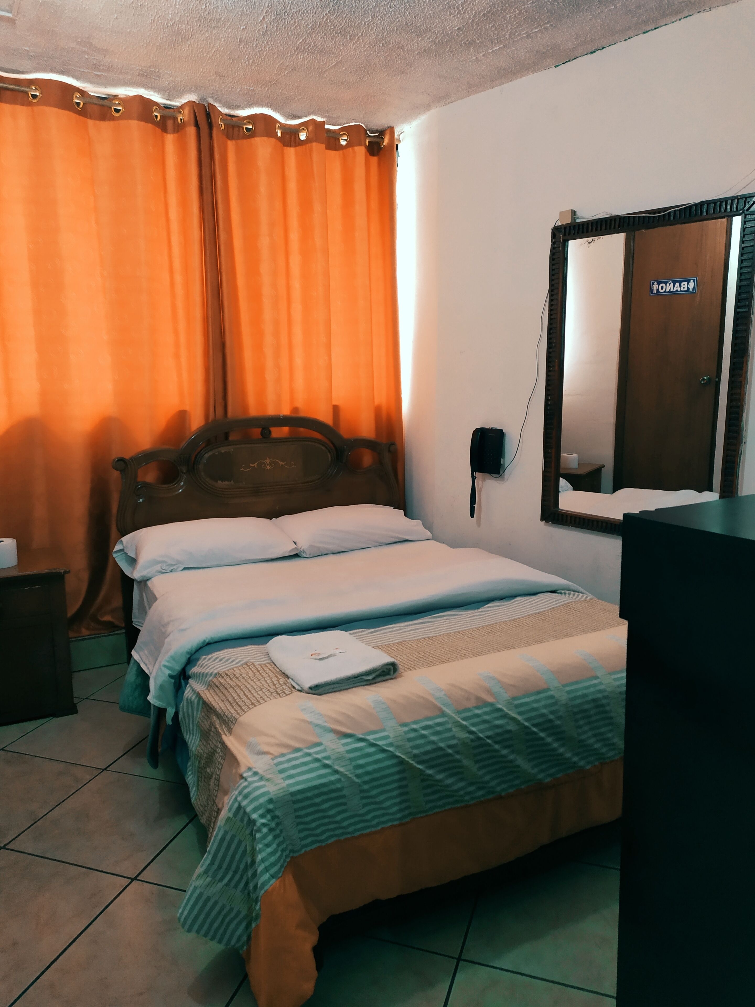 Ein Hotelzimmer mit Bett, Nachttisch mit Lampe, Spiegel und Tür mit Schild.