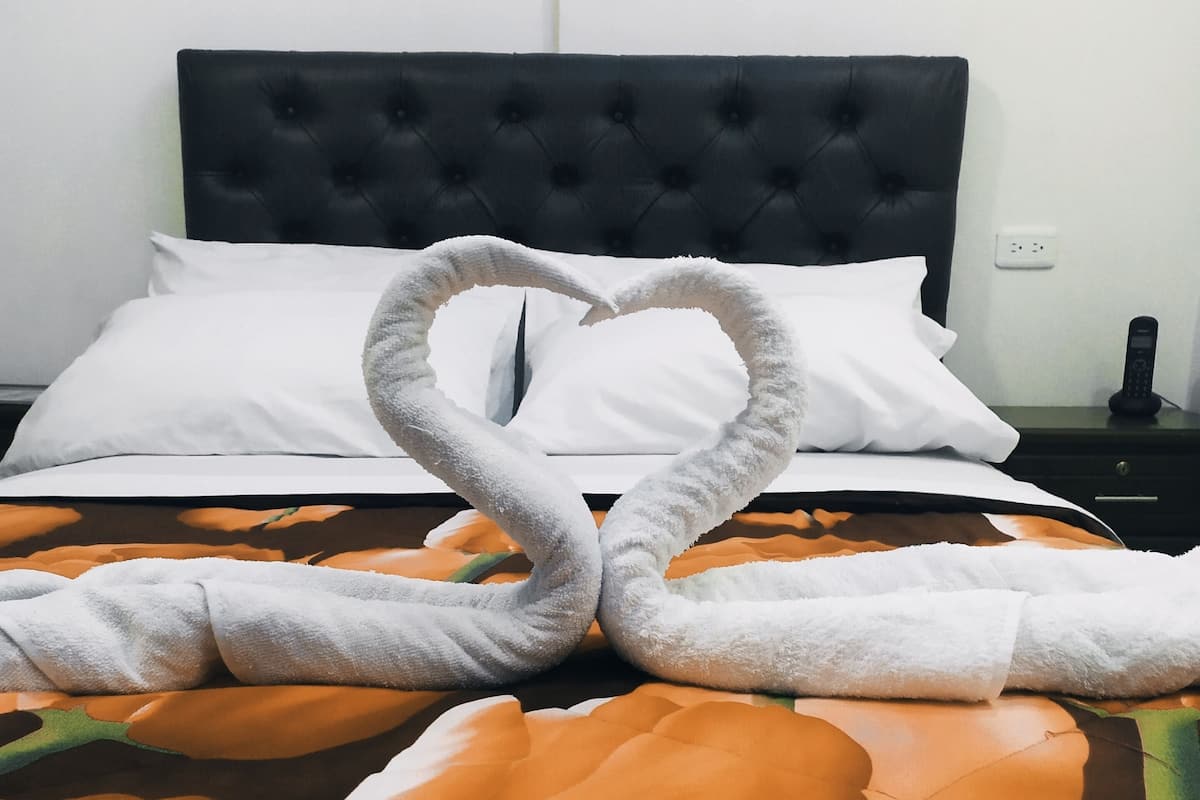 A bed with a floral bedspread, a heart-shaped towel arrangement, and a black headboard.