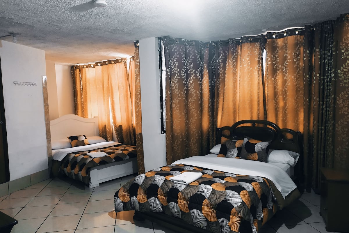 A hotel room with two beds, a tiled floor, and curtains with a leaf pattern.