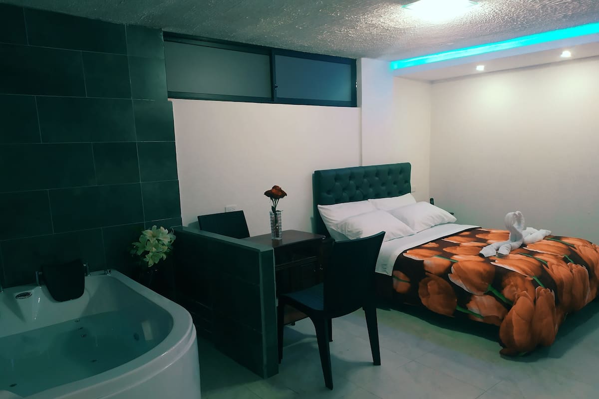 A bedroom with a bed, a desk, a chair, a bathtub, and a window.