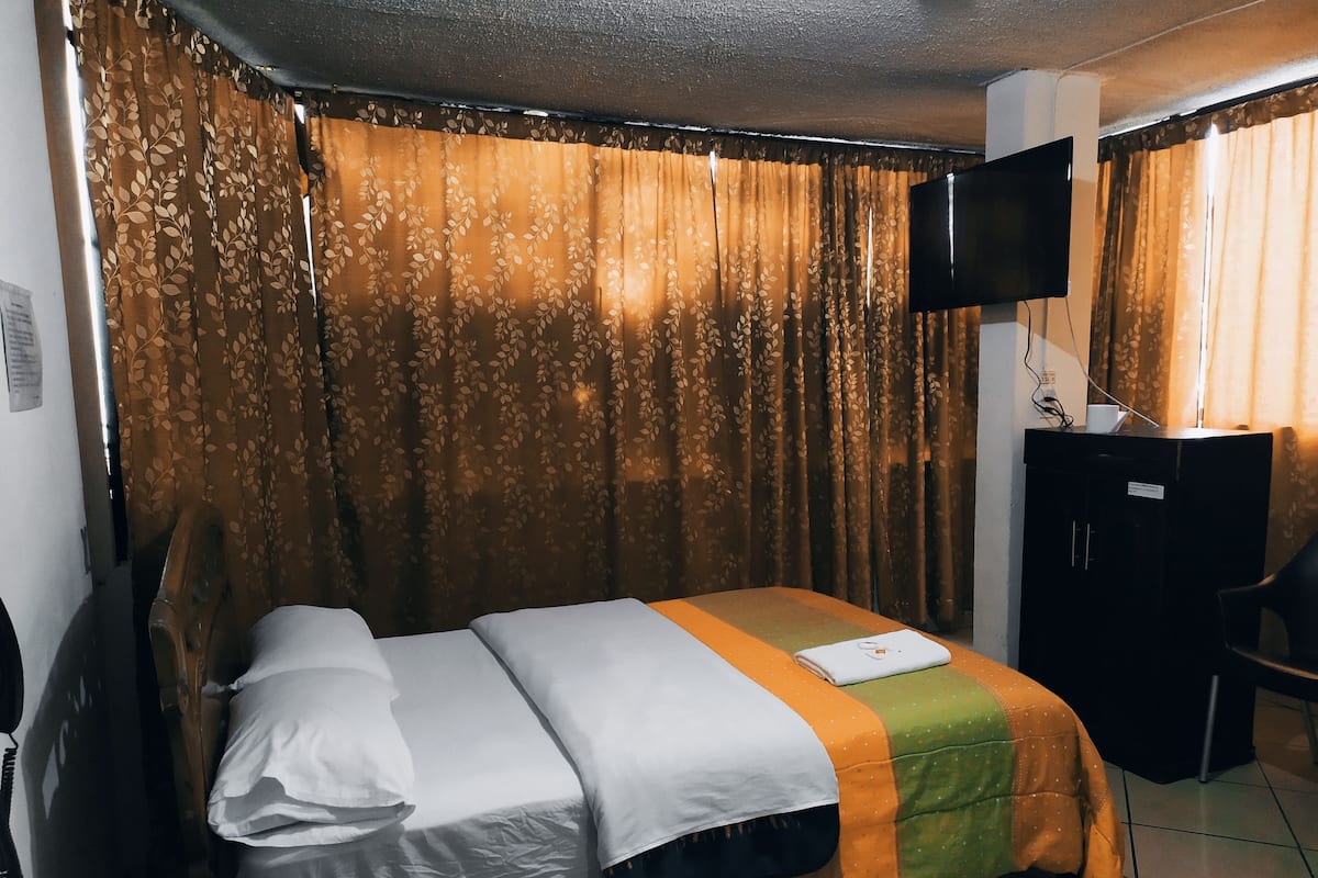 A hotel room with a bed, a desk, a chair, a television, and curtains.