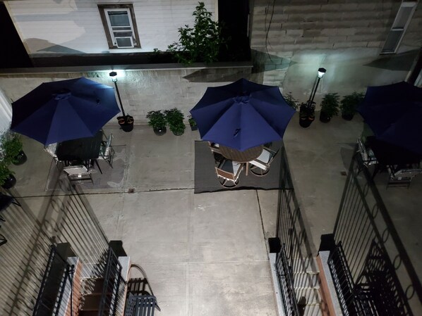 An outdoor patio area with tables and chairs under blue umbrellas, surrounded by potted plants and a building with a stone facade.