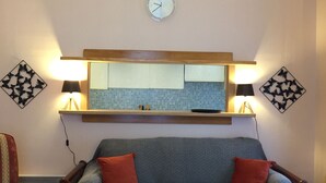 Una sala de estar con un sofá, dos sillones, un reloj de pared y dos lámparas de pared.