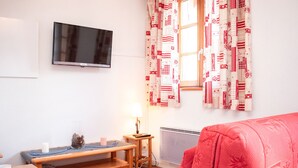 Ein gemütliches Wohnzimmer mit einem roten Sofa, einer Holzbank, einem an der Wand montierten Fernseher und gemusterten Vorhängen.