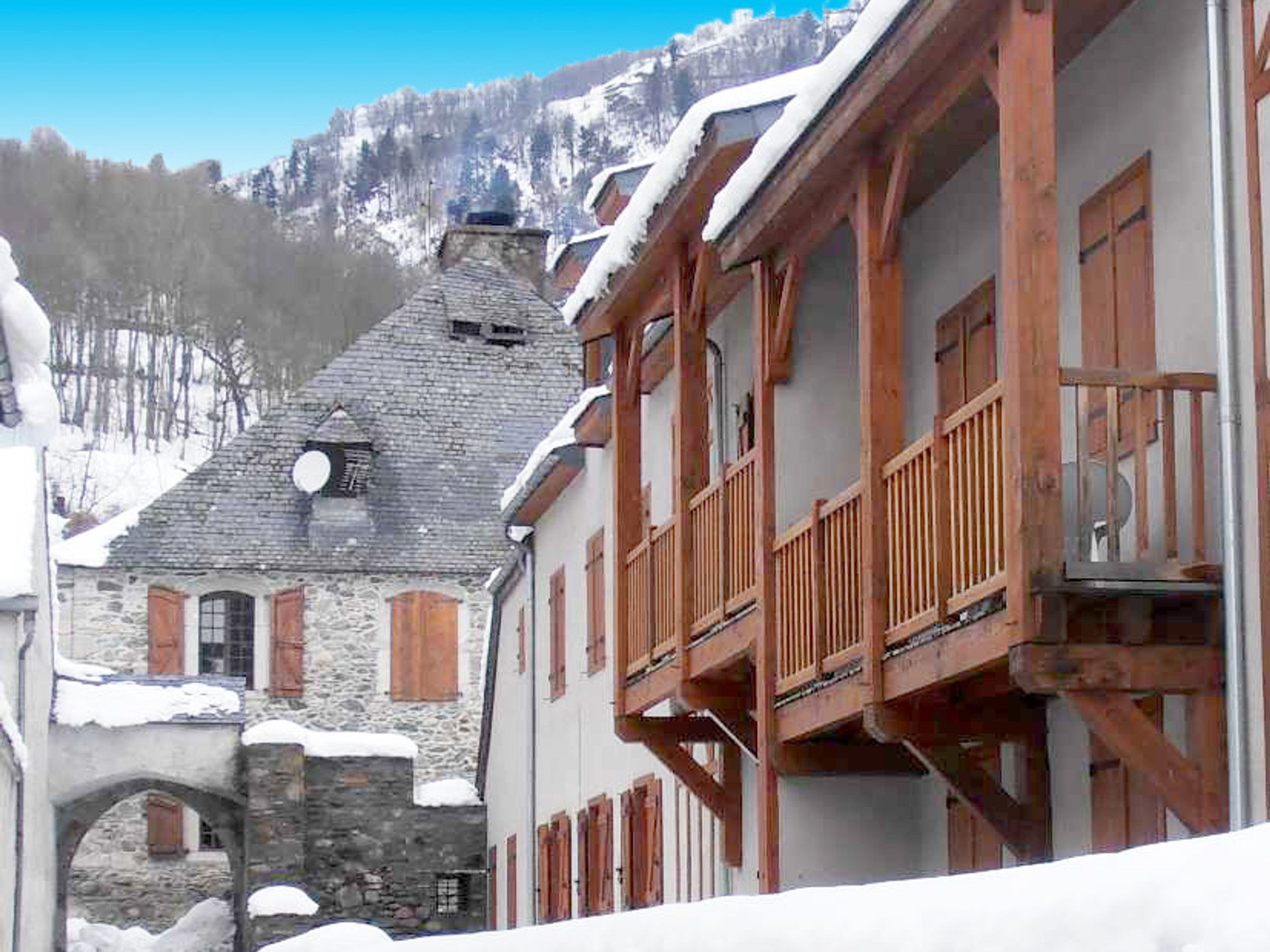 A traditional stone building with wooden balconies and a snow-covered mountain backdrop.