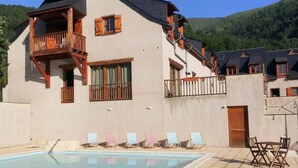 Ein Gebäude mit Swimmingpool, einem Balkon mit Holzbalkonen und Blick auf grüne Hügel.