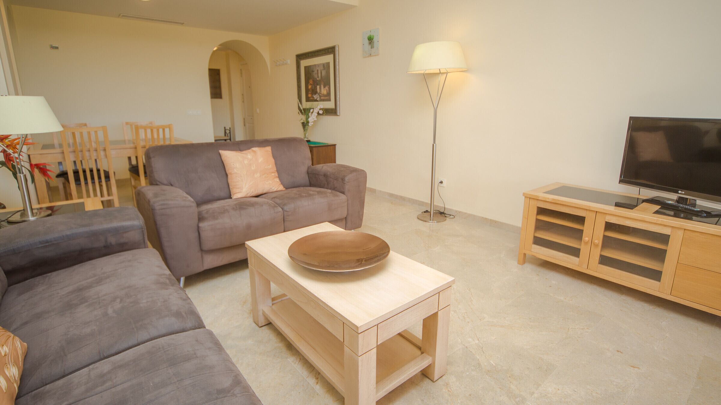 A living room with a grey sofa, a wooden coffee table, a TV stand with a flat-screen TV, and a floor lamp.