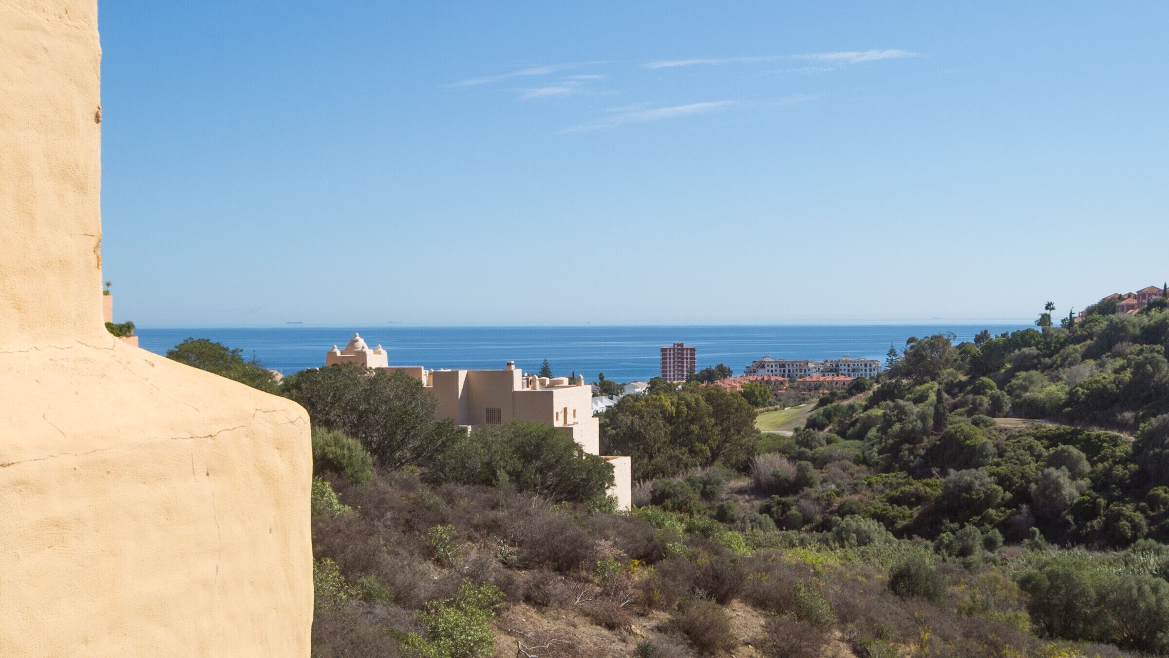 Paisagem costeira com edifícios, vegetação e uma vista clara do mar.