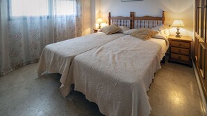 A double bed with a wooden headboard, two bedside tables with lamps, and a floral-patterned curtain. - Dorasal Bl. A esc. IV 1º Solo Familias! (Xeraco Playa)