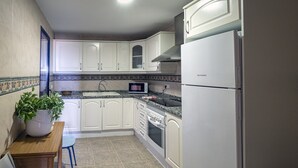 A kitchen with white cabinets, a microwave, a stove, and a refrigerator. - Dorasal Bl. A esc. IV 1º Solo Familias! (Xeraco Playa)