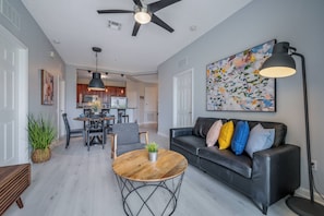 A modern living room with a black leather sofa, a wooden coffee table, and a dining area with a chandelier. - IS1-208 - Lake View Corner Unit - Modern Decor (Orlando)