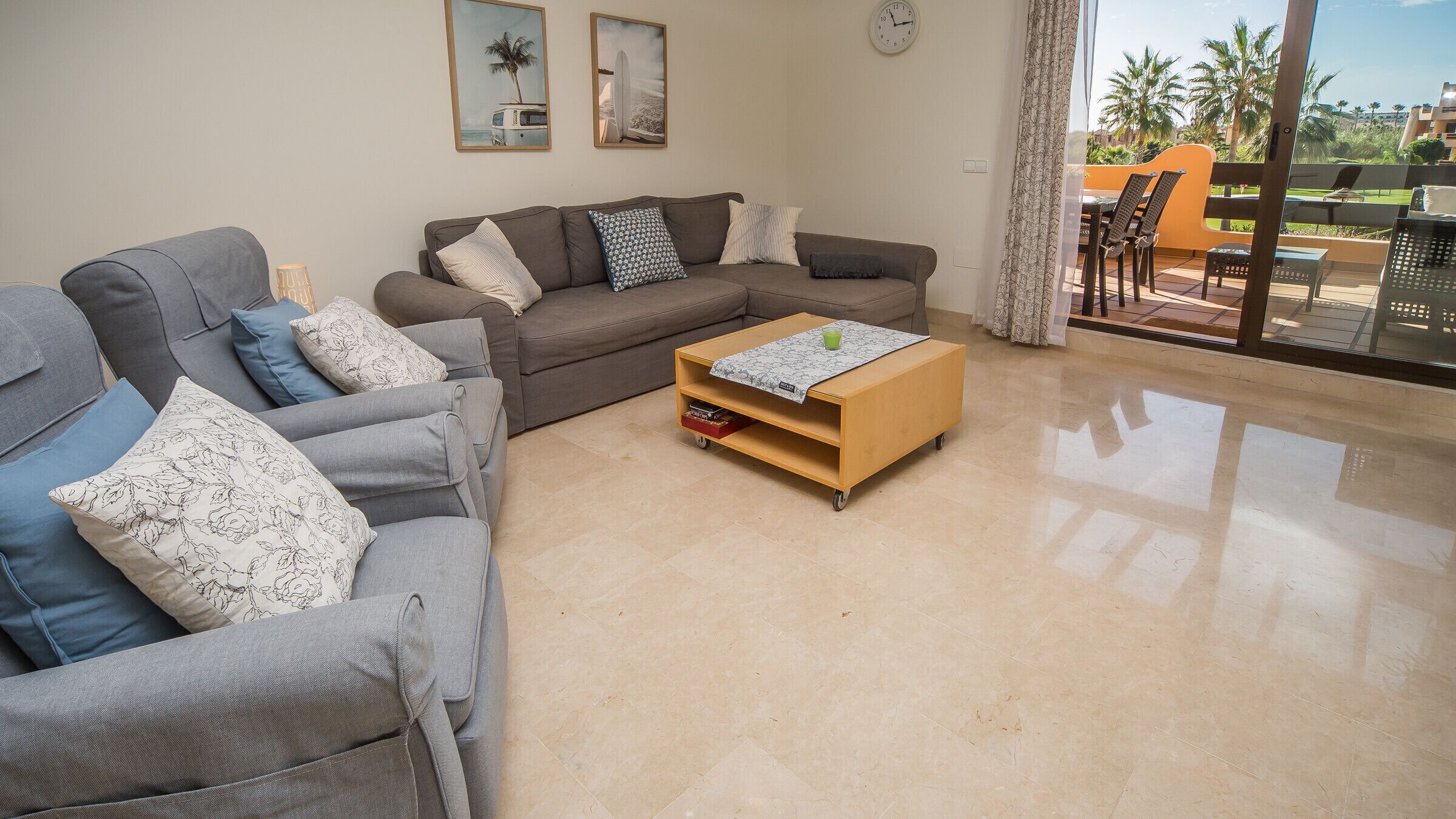 Ein Wohnzimmer mit zwei grauen Sofas, einem Holztisch und Blick auf eine Terrasse mit Gartenmöbeln.