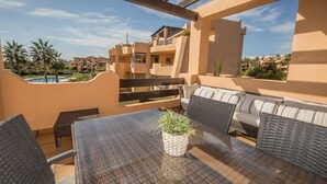 Patio esterno con tavolo e sedie, una pianta in vaso e vista su una piscina e altri edifici.