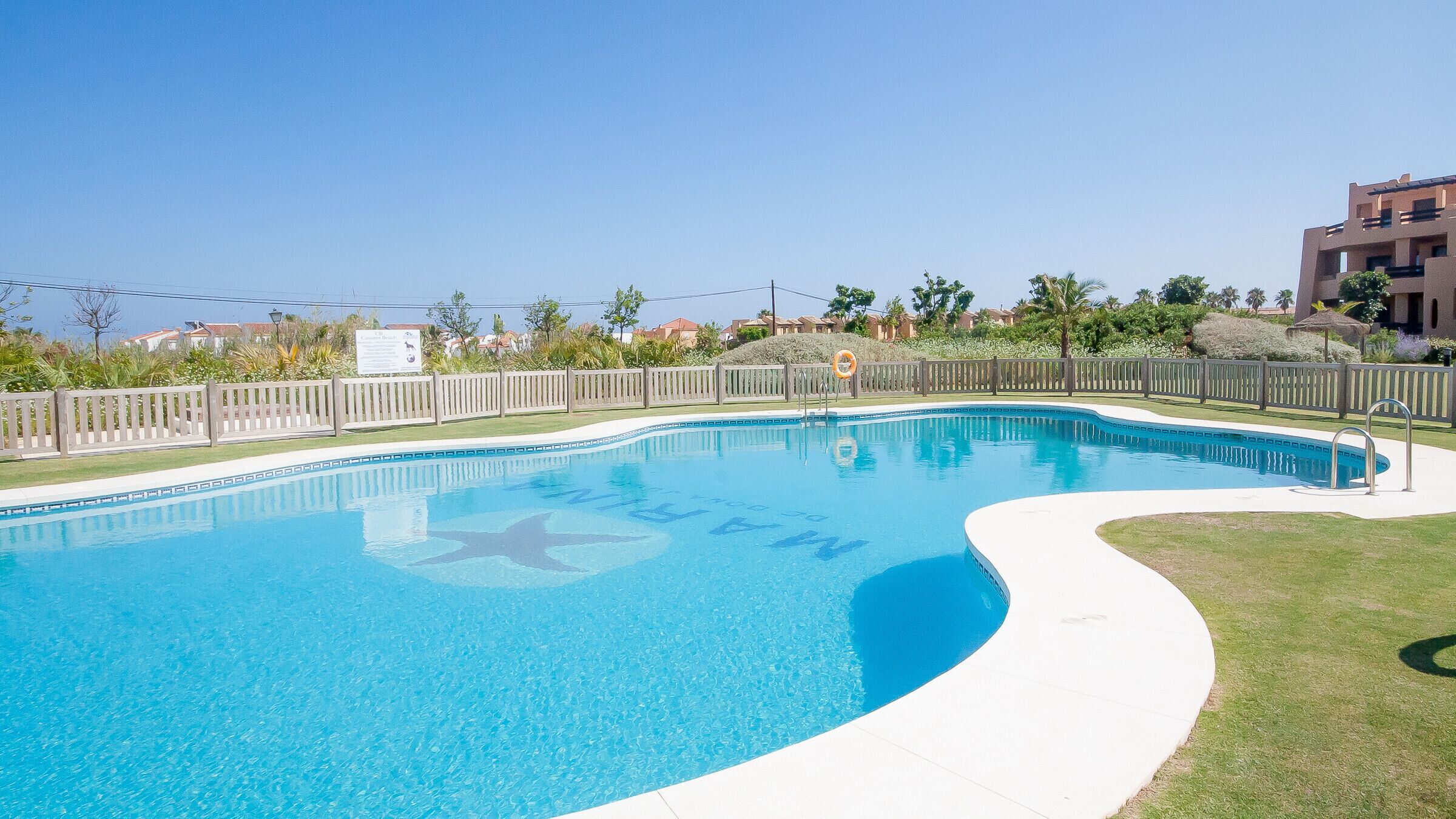 Una piscina azul cristalina con cubierta de madera y un puesto de socorrista.