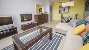 Un salon avec un téléviseur, des meubles en bois, un canapé et un tapis à motifs.