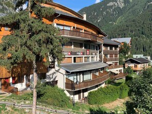 Un edificio in legno su più piani con balconi, circondato da alberi e montagne.