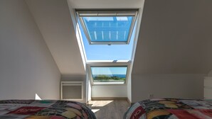 A bedroom with two beds, a skylight, and a view of the outdoors.