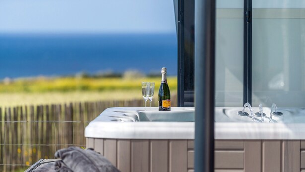 A hot tub with a bottle of champagne and two glasses on a balcony overlooking the ocean.