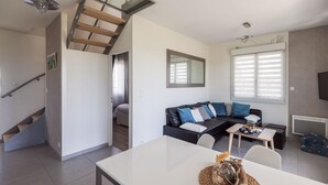 A modern living space with a staircase, a sofa set, a dining table, and a kitchen area.