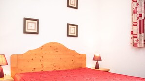 A room with a wooden headboard bed, a red bedspread, two bedside lamps, and two framed pictures on the wall. - 2-Room Apartment for 4 in Vignec (Vignec)