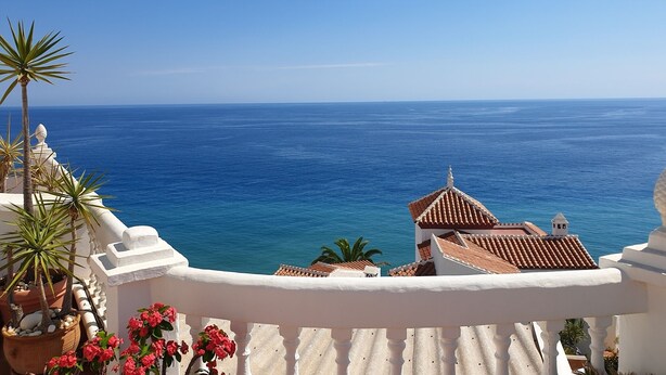 A coastal view with a white balcony, terracotta roof buildings, and a clear blue sea. - Spacious and bright penthouse with panorama seaview (Nerja)