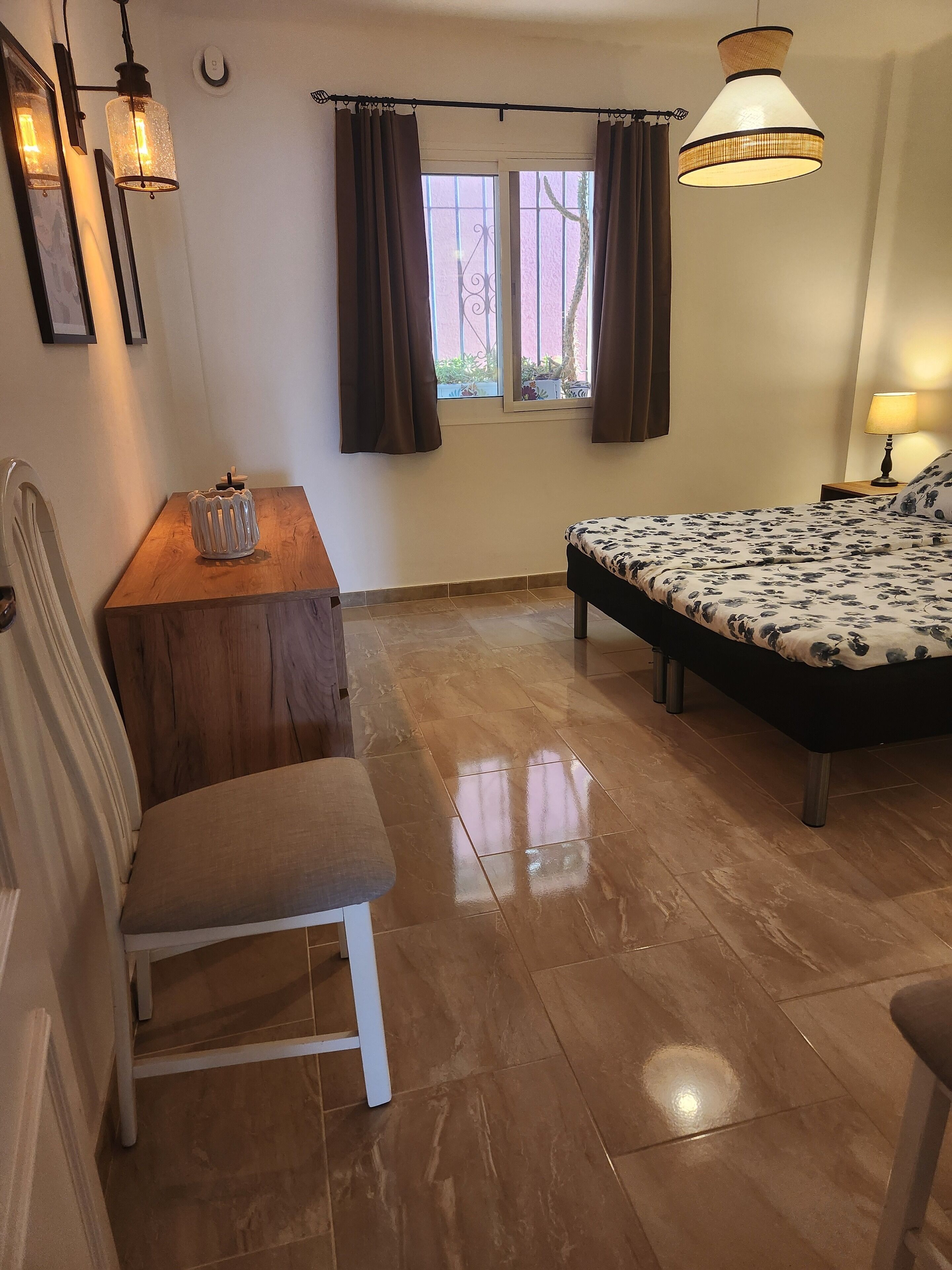 A bedroom with a bed, a desk, a chair, and a window with curtains.