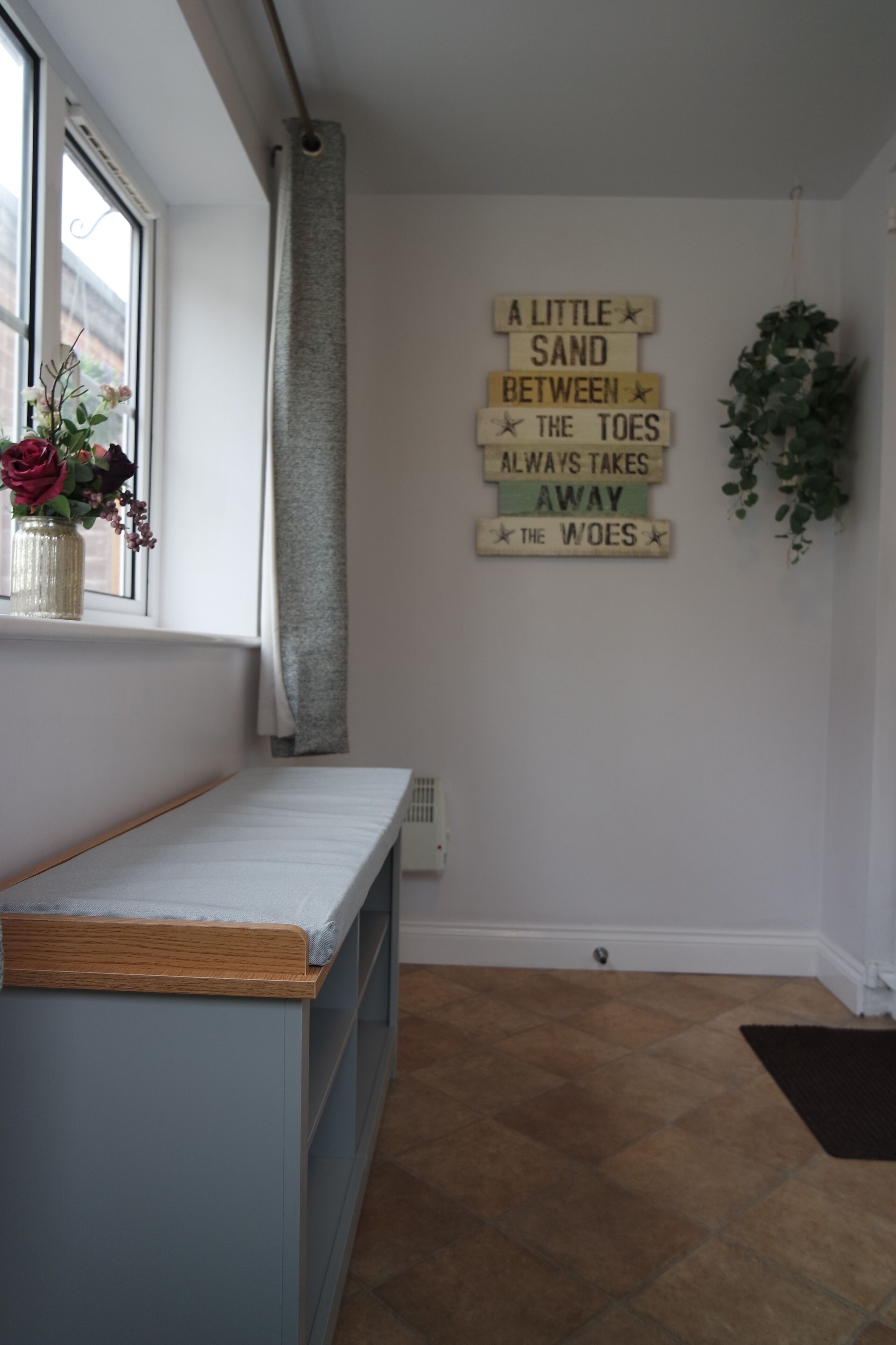 Una habitación con ventana, un banco de madera, un letrero en la pared y una planta en maceta.