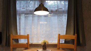 Un coin repas avec une table ronde, deux chaises en bois, un luminaire suspendu et une fenêtre avec des rideaux.