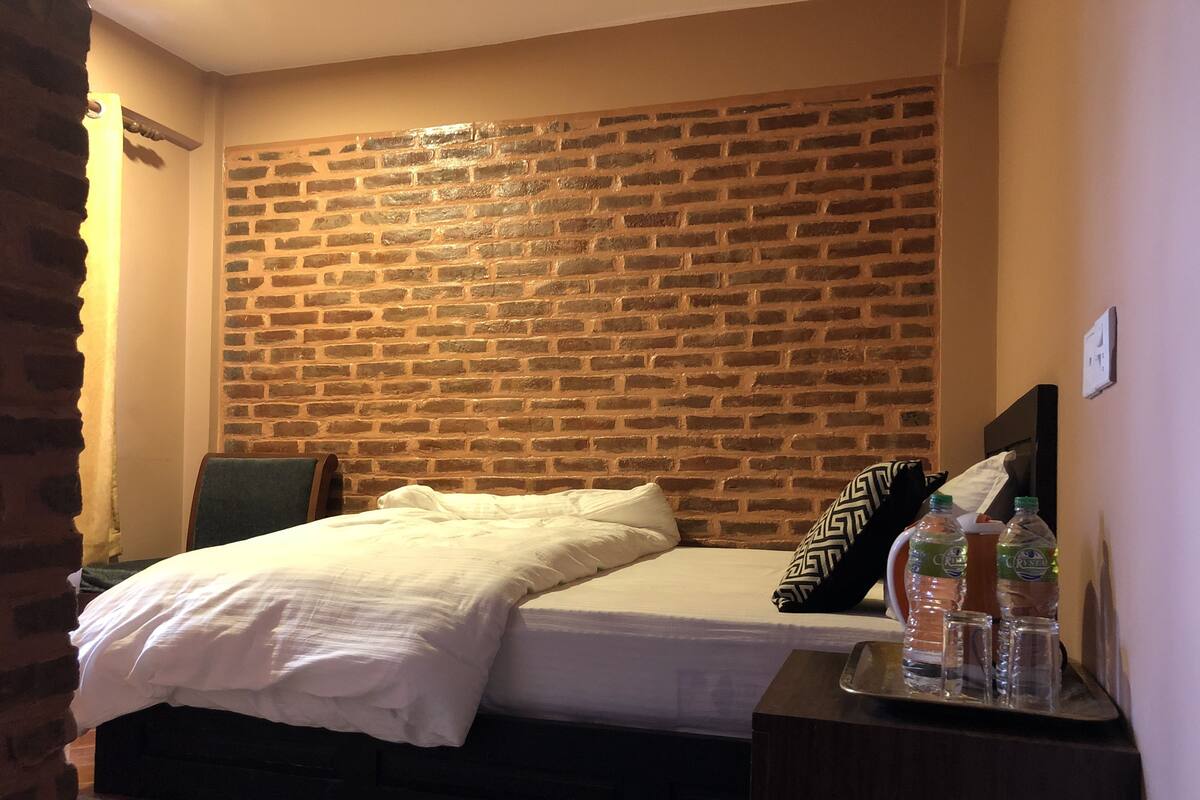Un dormitorio con cabecera de ladrillo, una cama con ropa de cama blanca y una mesita de noche con botellas de agua.