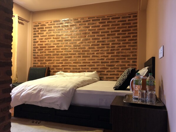 Une chambre à coucher avec une tête de lit ornée d’un motif en briques, un lit avec une literie blanche et une table de chevet sur laquelle sont posées des bouteilles d’eau.