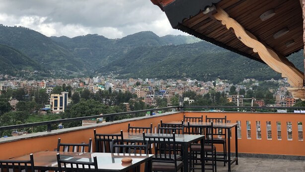 Terraza en la azotea con mesas y sillas, con vistas a un paisaje urbano y montañas.