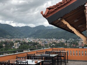 A rooftop terrace with tables and chairs, overlooking a cityscape and mountains. - Tashi Delek Guest House (Bhaktapur)