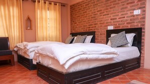Una cama doble con estructura de madera y cabecera negra, dos almohadas con diseños geométricos, una mesita de noche de madera y un pequeño estante de madera.