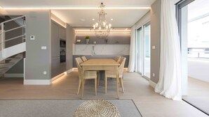 A modern kitchen with a marble countertop, a dining area with a wooden table and chairs, and a staircase on the left.