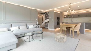A modern living room with a sectional sofa, a dining area with a wooden table and chairs, and a kitchen with a marble backsplash.