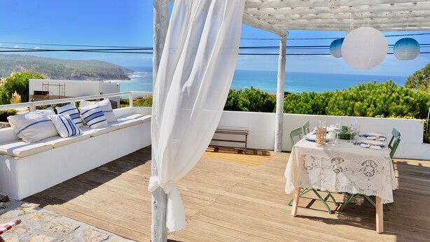 A terrace with a white canopy, a table set for dining, and a view of the ocean.