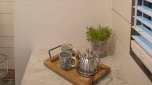 Et køkken med træhylder med tallerkener og planter, en bakke med te og kopper, og et vindue med skodder.