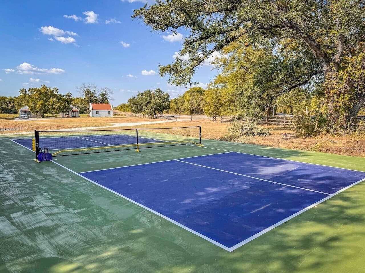 A tennis court with a net, surrounded by trees and a building in the background.