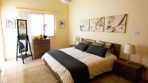 A bedroom with a bed, bedside tables, a dresser, a mirror, and artwork on the wall.