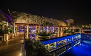 Een resort met een gebouw met rieten dak, een zwembad en buitenzitplaatsen.