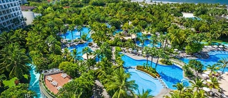 Un complexe hôtelier doté de plusieurs piscines, entouré d’une végétation luxuriante et de palmiers.