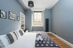 Cozy retreat with a large bed, bookshelf, and chandelier.