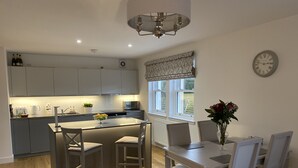 A modern kitchen with grey cabinets, a central island with bar stools, a dining table with chairs, and a clock on the wall. - Luxury flat (St Andrews)