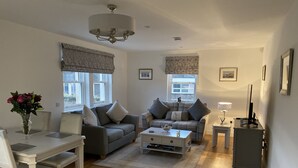 A living room with a sofa, a coffee table, a dining table with chairs, a TV stand, and a lamp. - Luxury flat (St Andrews)