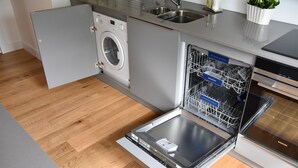 A compact kitchen with a built-in washer and dishwasher, wooden flooring, and a stainless steel sink. - Luxury flat (St Andrews)