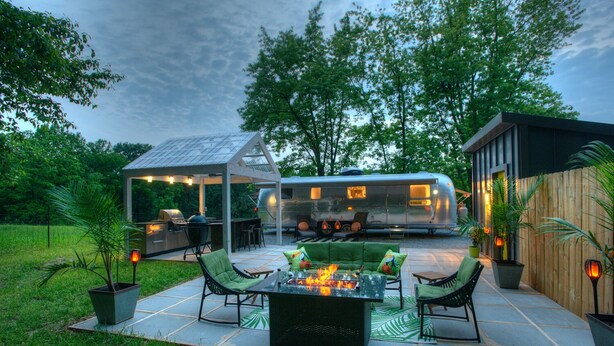 An outdoor patio with a fire pit, green seating, and a covered grill area.