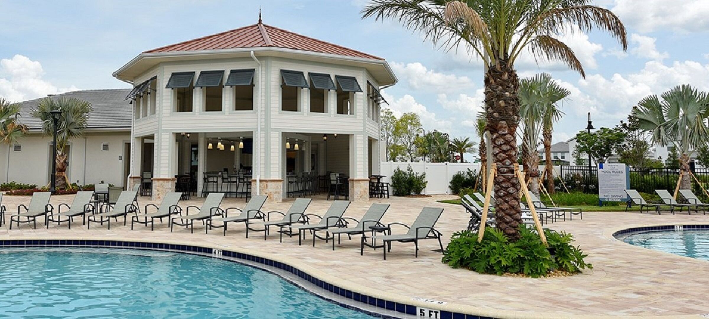 Un área junto a la piscina con sillones de descanso, un espacio de estar cubierto y una piscina.