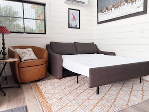 Una habitación moderna con un sofá, una silla, un tapete y dos cuadros en la pared.